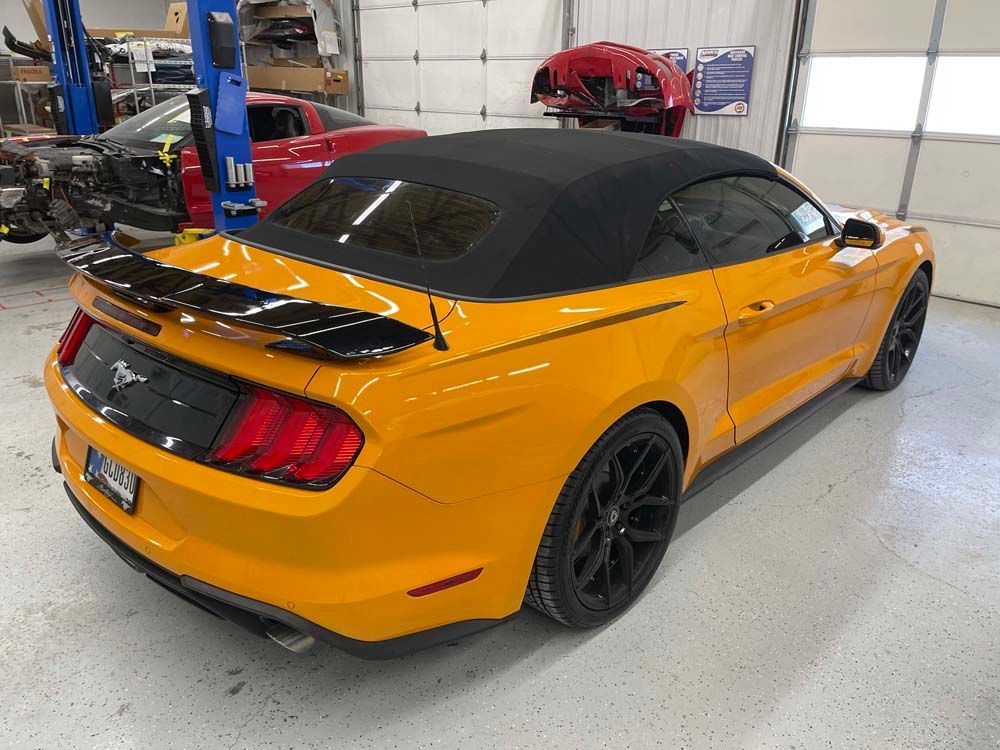 A yellow mustang convertible is parked in a garage.