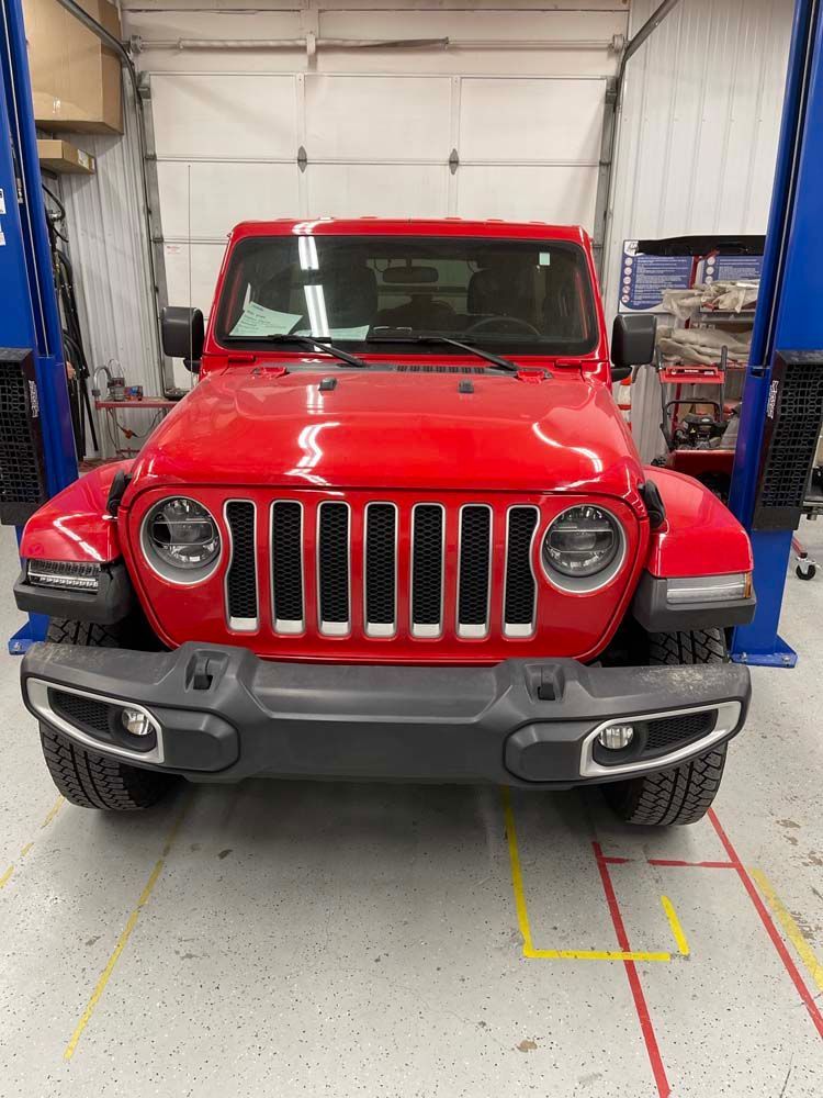 A red jeep is parked on a lift in a garage.