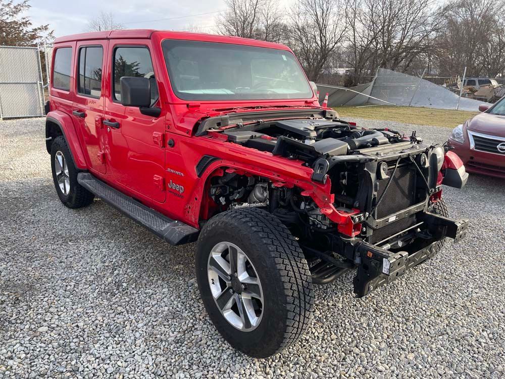A red jeep wrangler with the hood up is parked in a gravel lot.