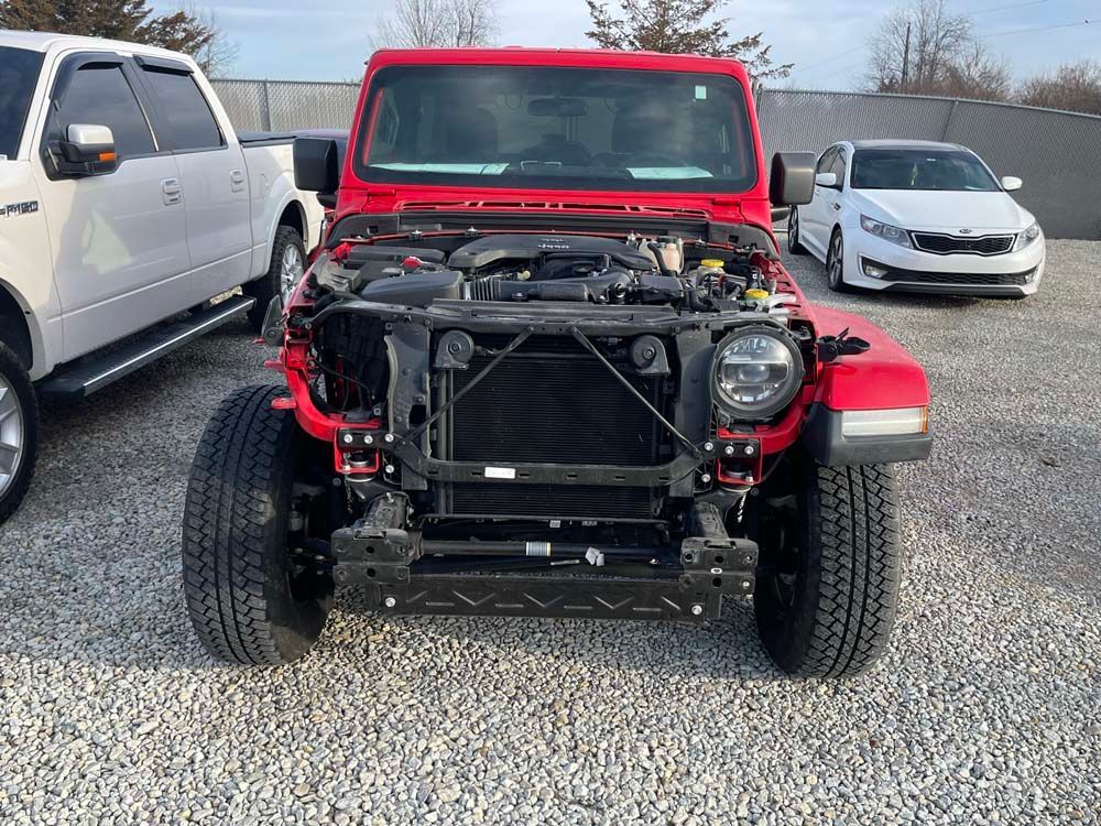 A red jeep with the hood removed is parked in a gravel lot.