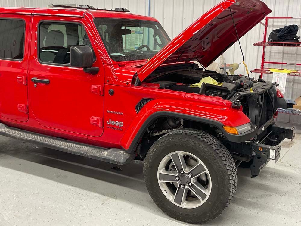 A red jeep with the hood up is parked in a garage.