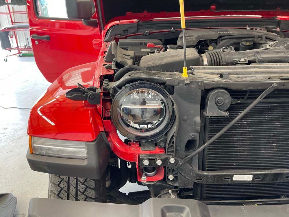 A red jeep with the hood open is sitting in a garage.