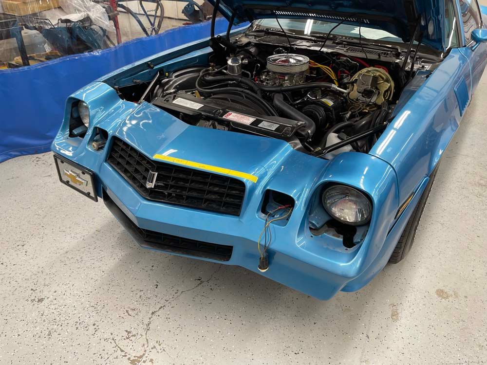 A blue car with the hood open is parked in a garage.