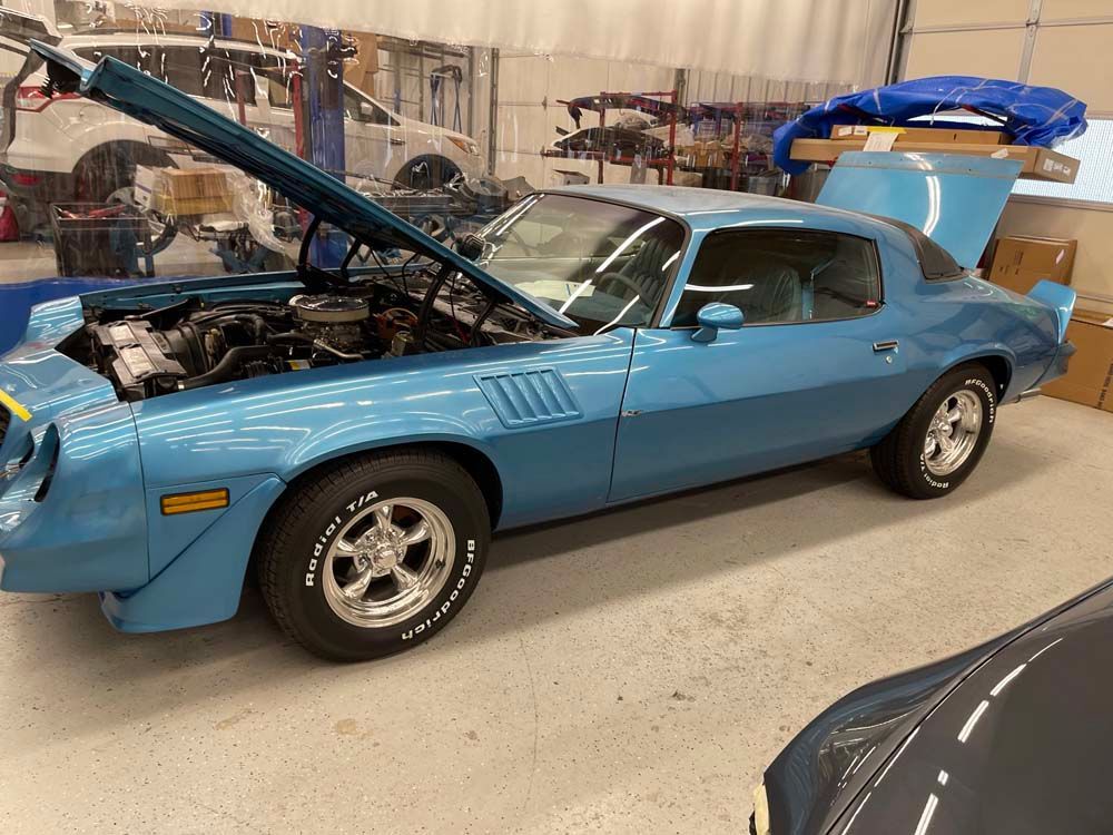 A blue car with the hood up is parked in a garage.