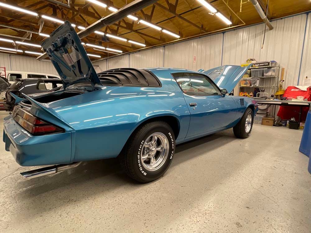 A blue car with the hood up is parked in a garage.