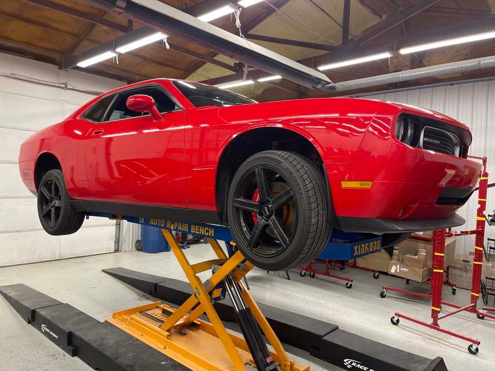 A red dodge challenger is sitting on a lift in a garage.