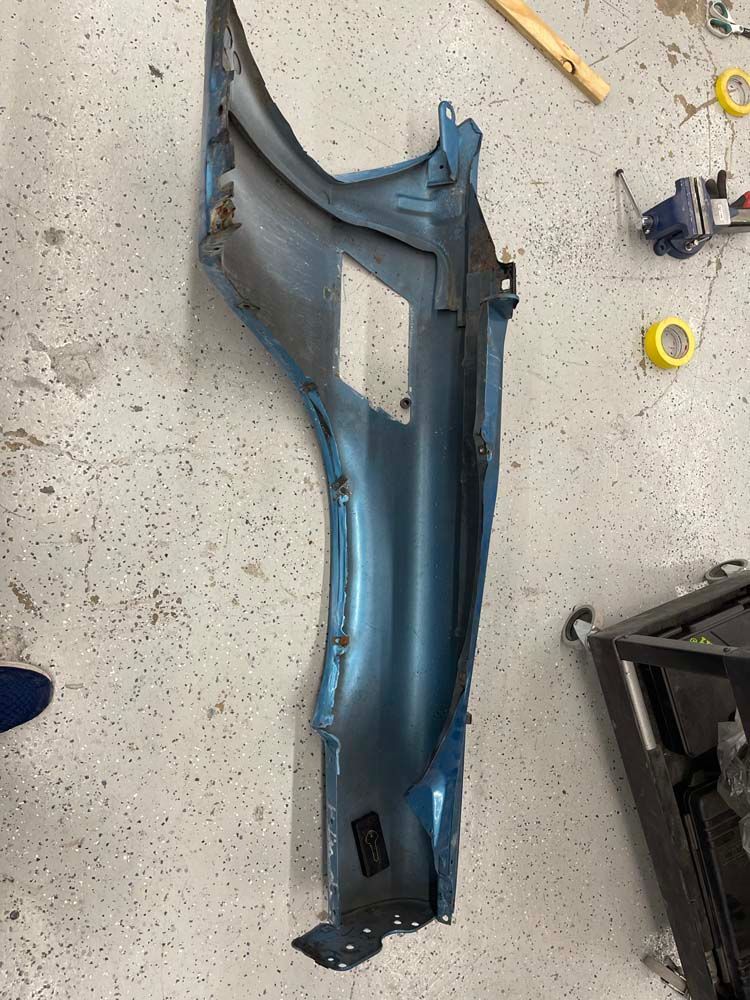 A blue fender is sitting on the floor next to a tape measure.