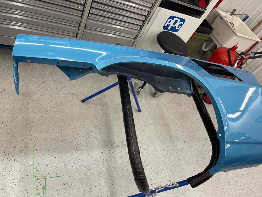 A blue car fender is sitting on a stand in a garage.