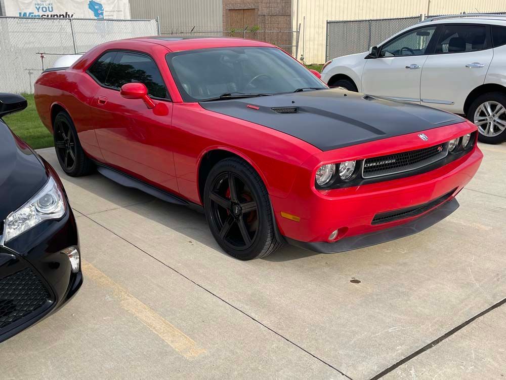 A red dodge challenger is parked in a parking lot next to a black car.