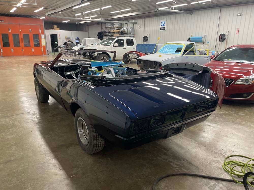 A blue convertible is sitting in a garage with other cars.