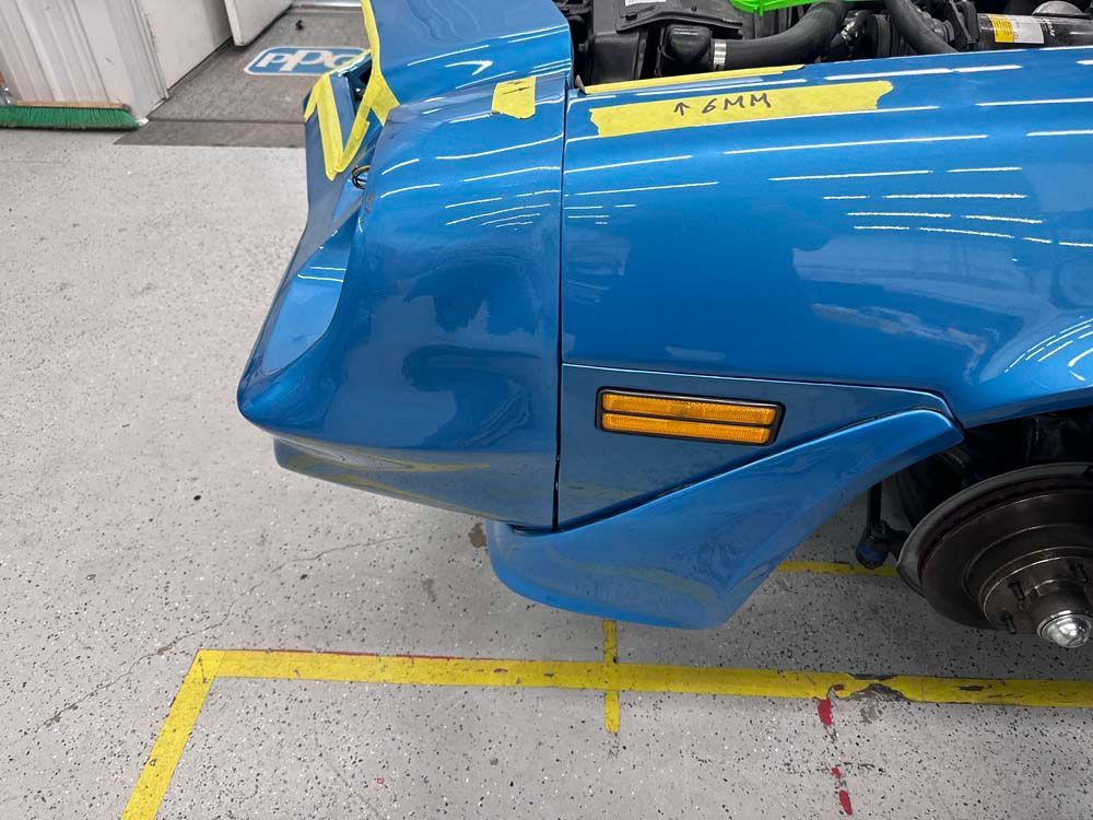 A blue car is sitting in a garage with a yellow sticker on the side that says ' why '
