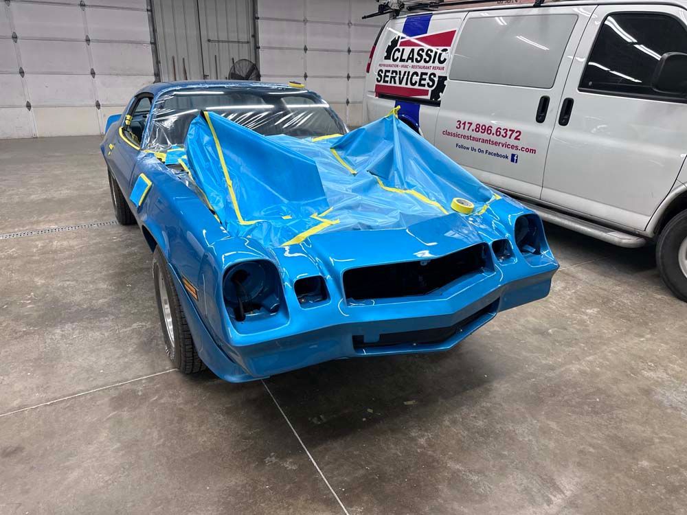 A blue car is sitting in a garage next to a white van.