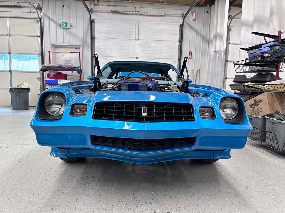 A blue car is parked in a garage with the hood up.