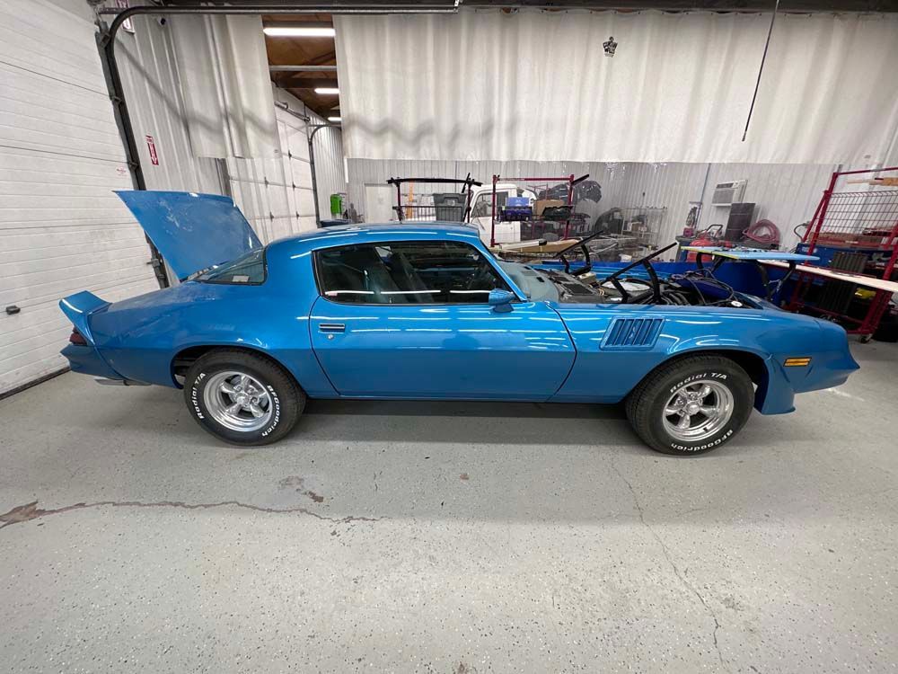 A blue car with the hood up is parked in a garage.