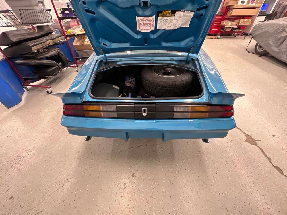 A blue car with the trunk open and a tire in it