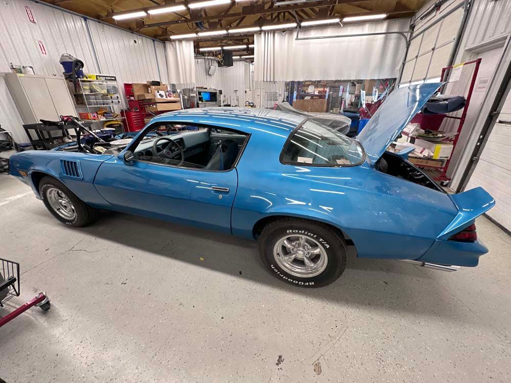 A blue car with the hood up is parked in a garage.