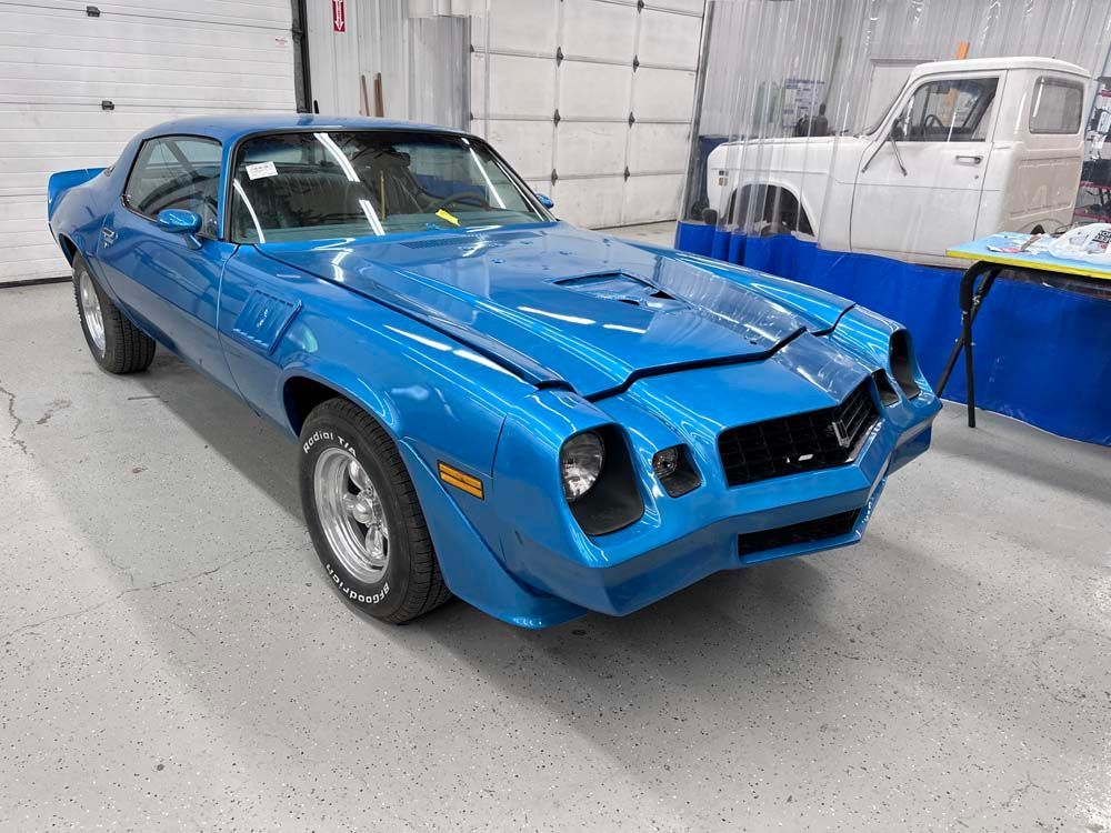 A blue car is parked in a garage next to a truck.