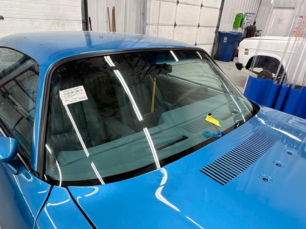A blue car with a yellow tag on the windshield is parked in a garage.