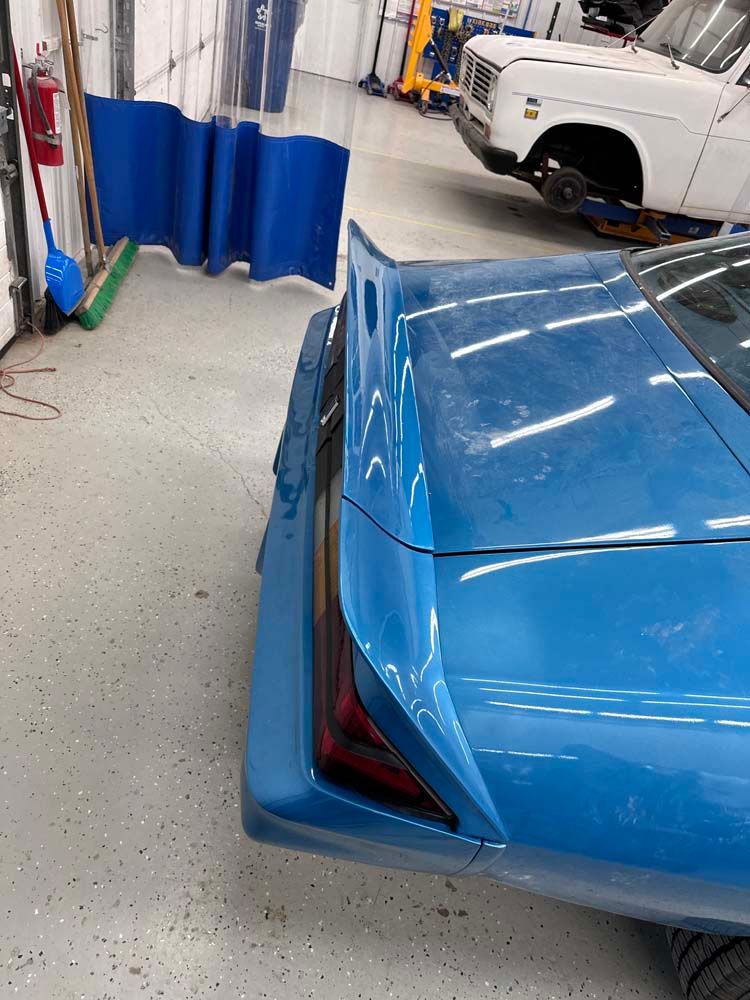A blue car is parked in a garage next to a white truck.