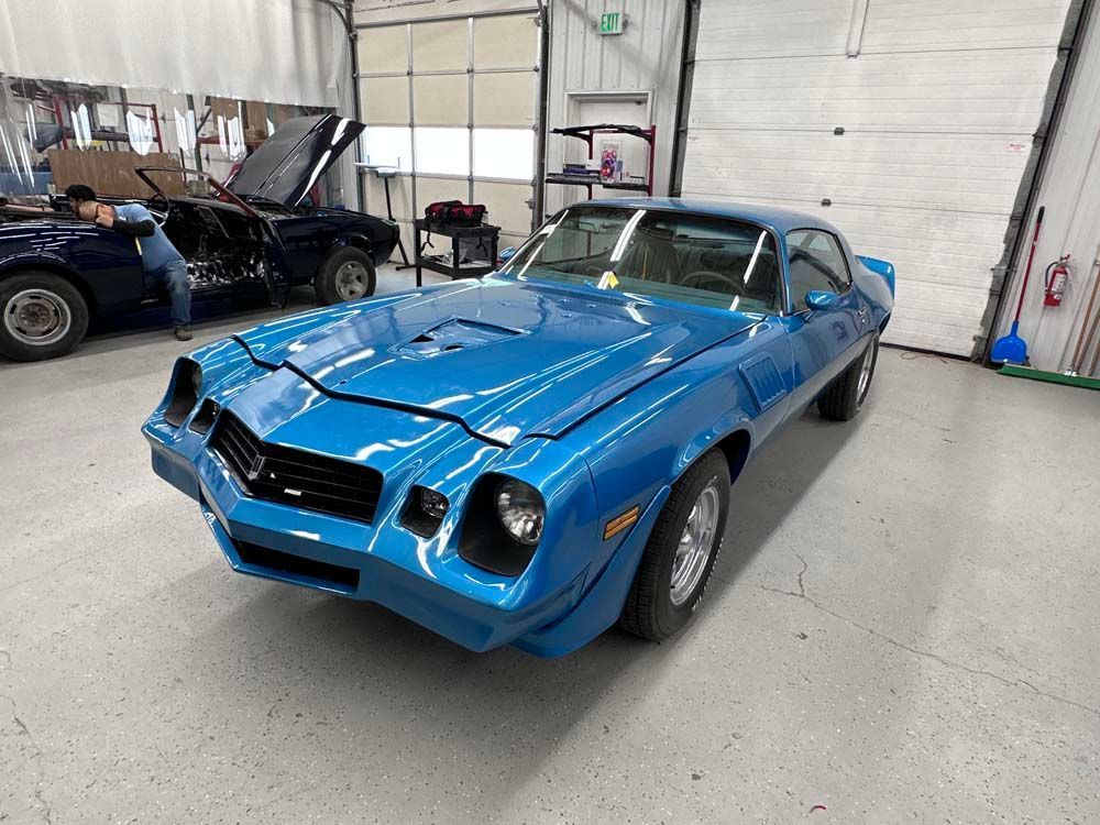 A blue car is parked in a garage with its hood up.