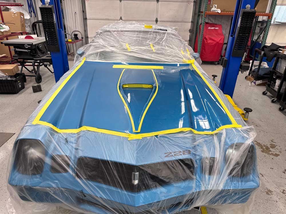 A blue car is wrapped in plastic and sitting on a lift in a garage.