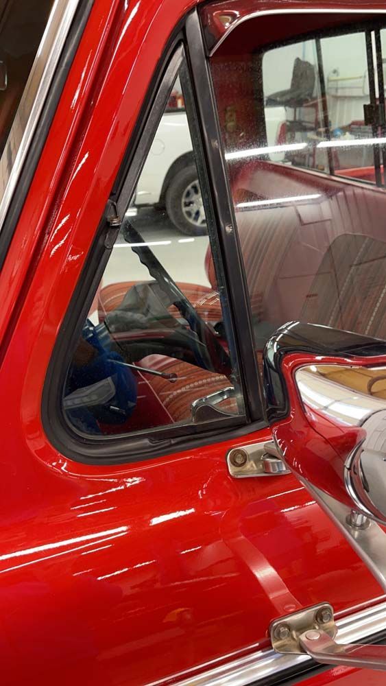 A red truck is parked in a garage with a reflection of a person in the window.