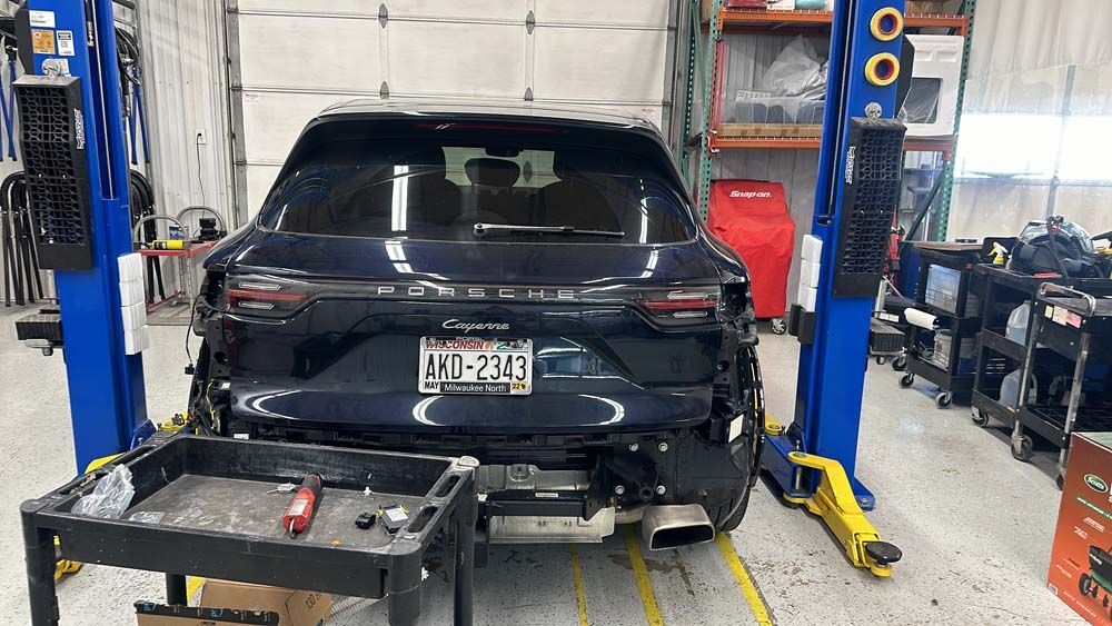 Dark blue SUV on a lift in a repair shop, rear bumper removed.