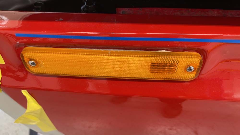 A close up of a red car with a yellow side light on it.