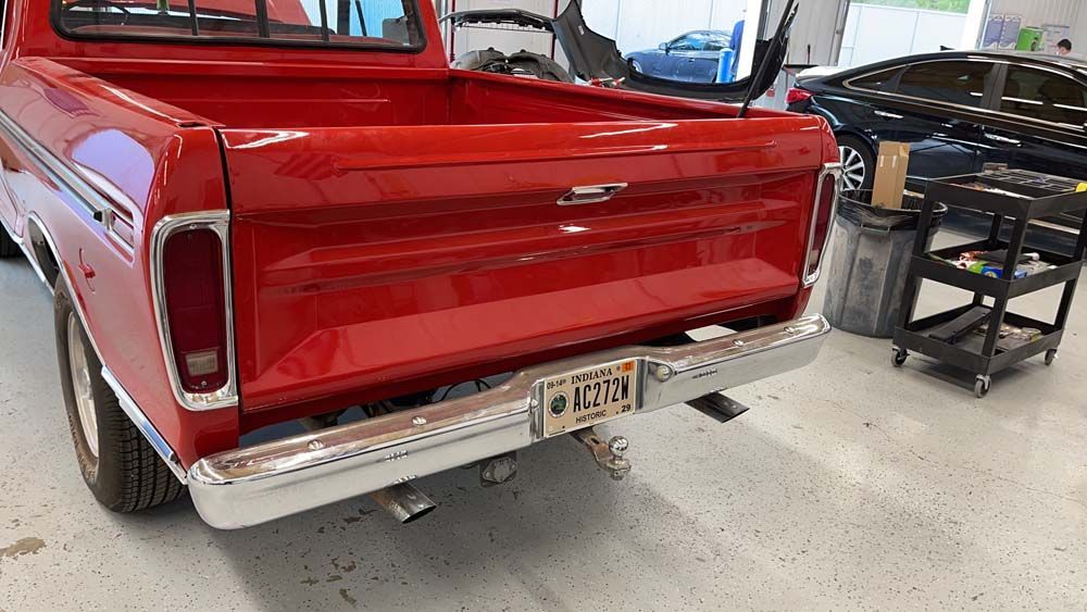 A red truck is parked in a garage next to a car.