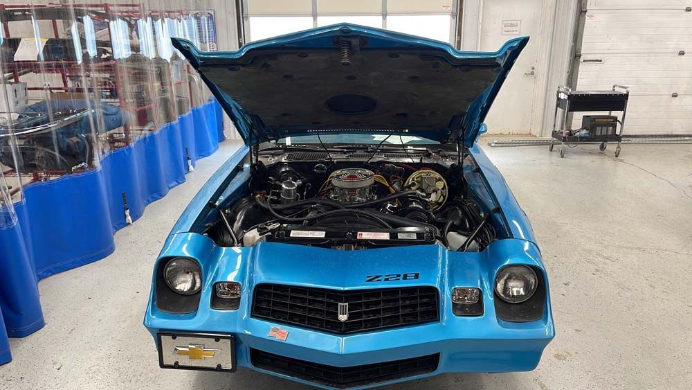 A blue car with the hood up is parked in a garage.