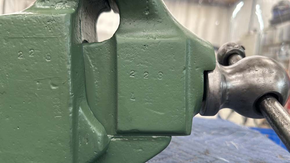 A close up of a green vise on a table.