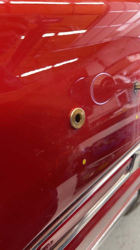 A close up of a red car door with a hole in it.