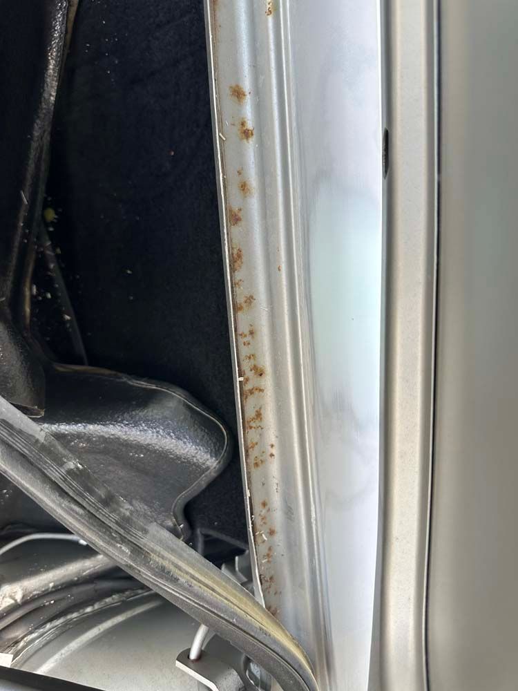 A close up of a car door with rust on it.