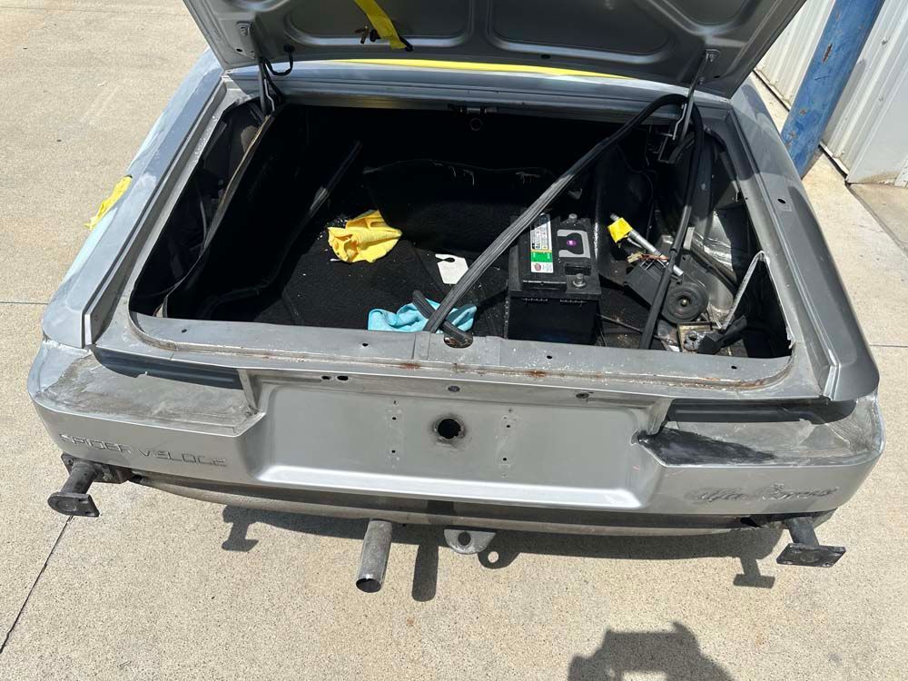 The trunk of a silver car with the hood up is empty.