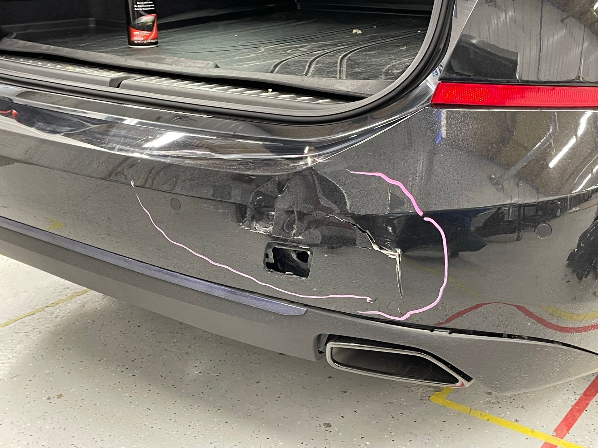 A black car with a damaged bumper is parked in a garage.