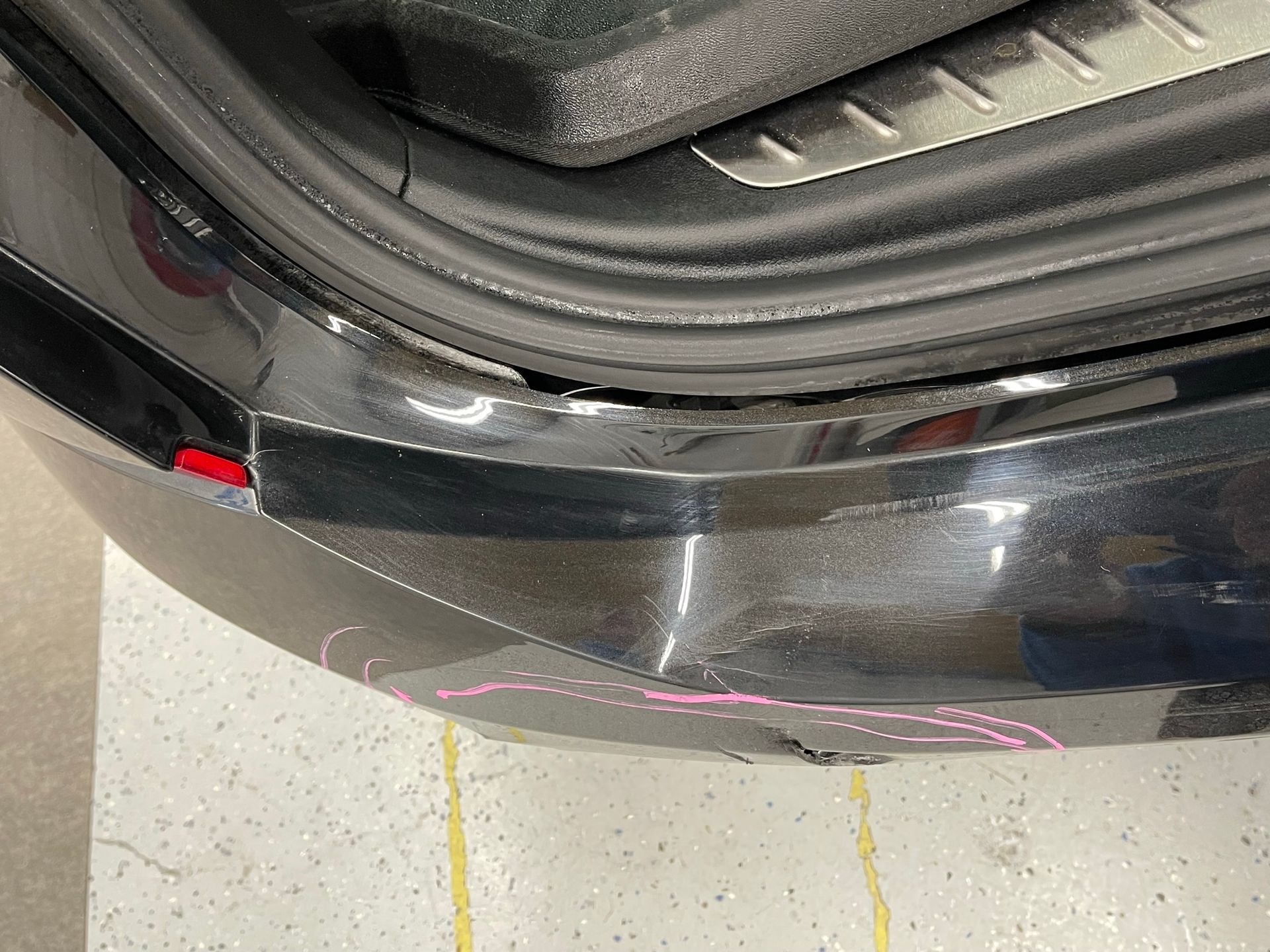 A black car with a damaged bumper is parked in a garage.