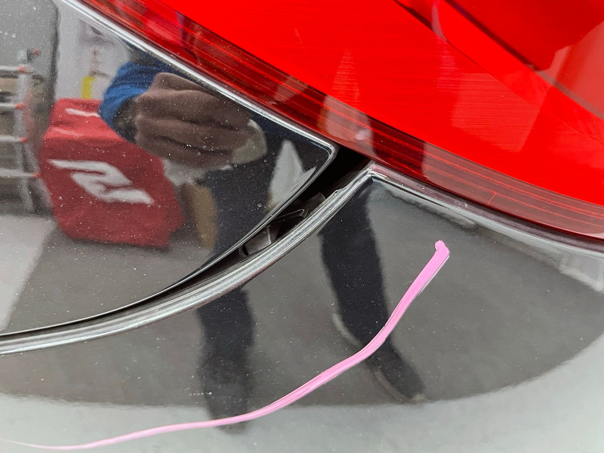 A person is taking a picture of their reflection in a red car.