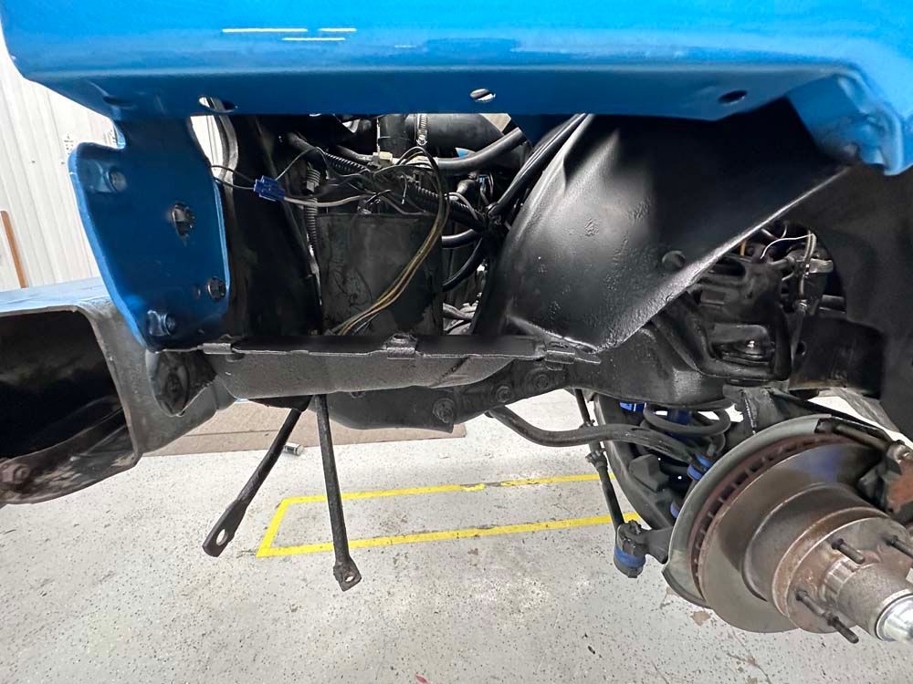 The underside of a blue car with a brake and a fender.