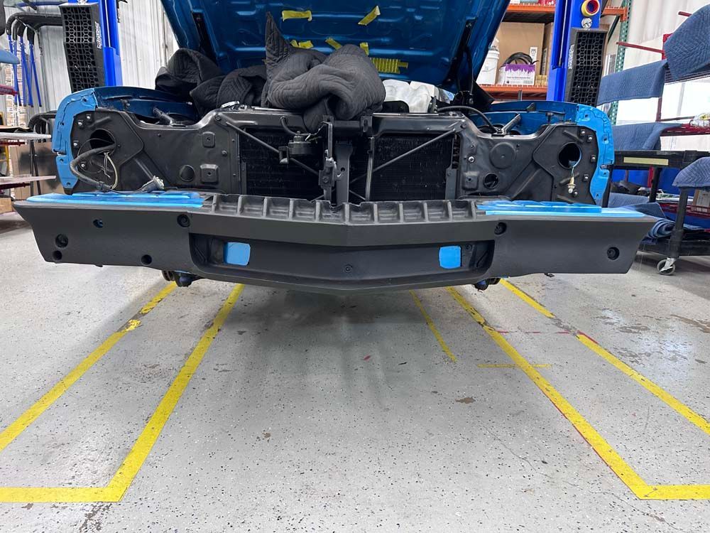 A blue car with the hood up is being worked on in a garage.