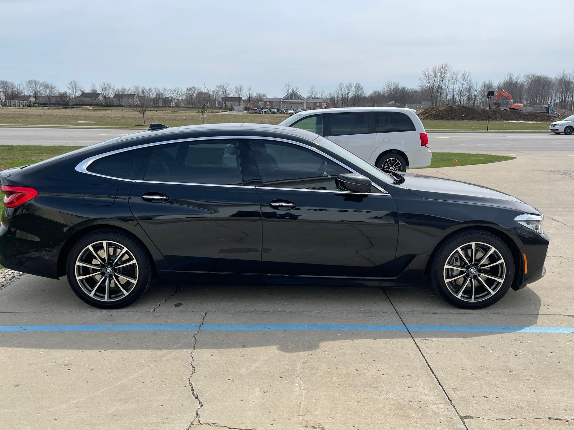 A black car is parked in a parking lot next to a white van.