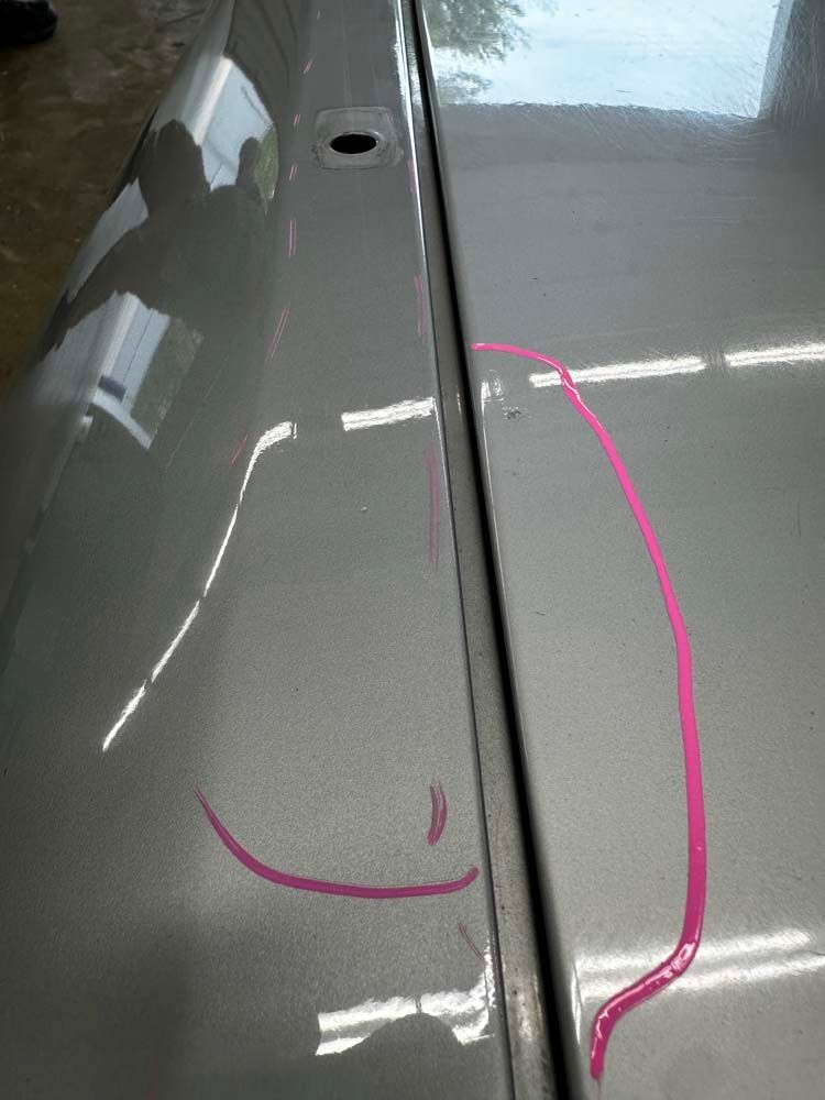 A close up of a car hood with a pink line drawn on it.