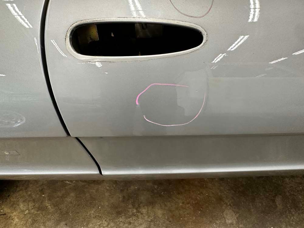 A close up of a silver car door with a hole in it