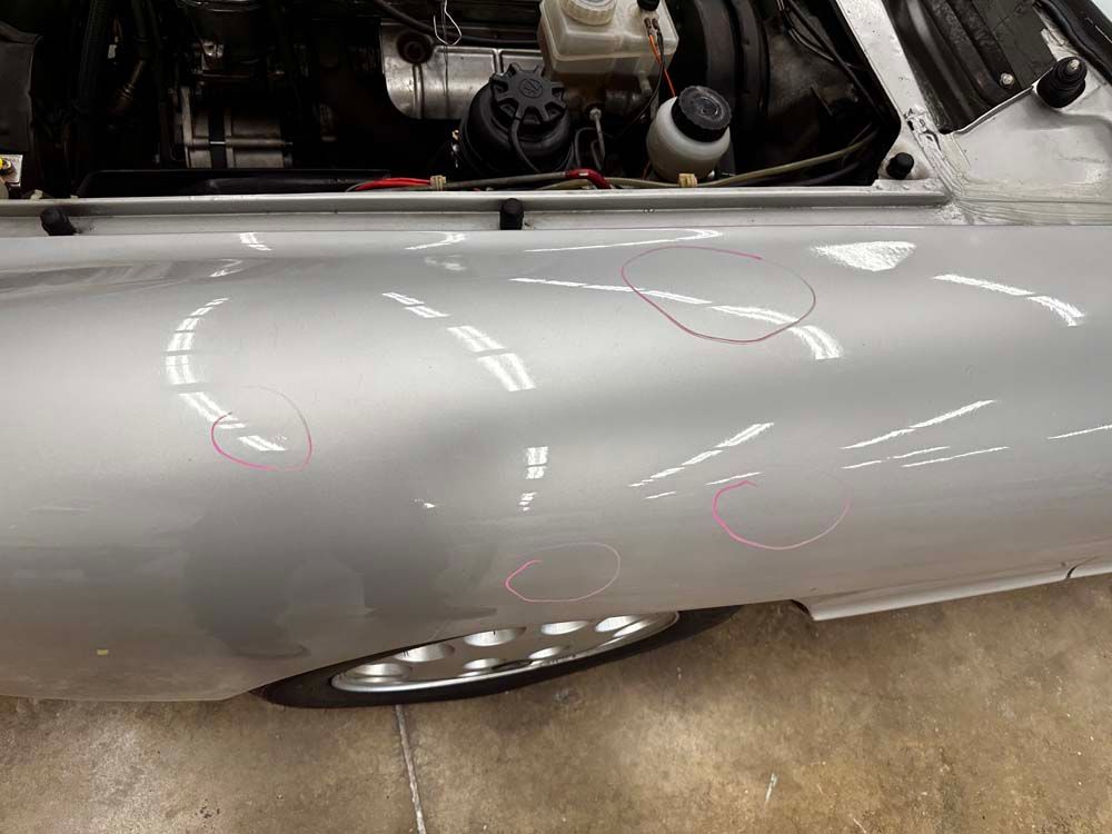 A silver car with the hood open is parked in a garage.