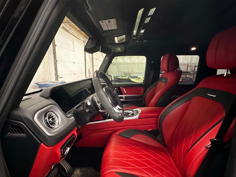 The interior of a black mercedes benz g63 amg with red seats.