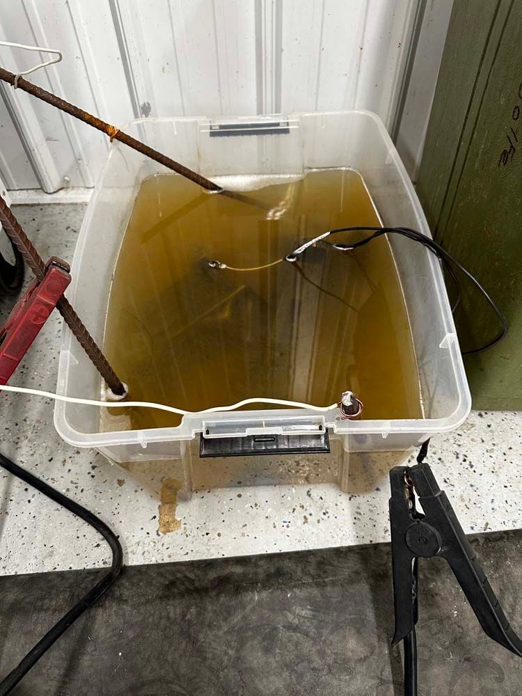 A clear plastic container filled with dirty water and welding supplies.