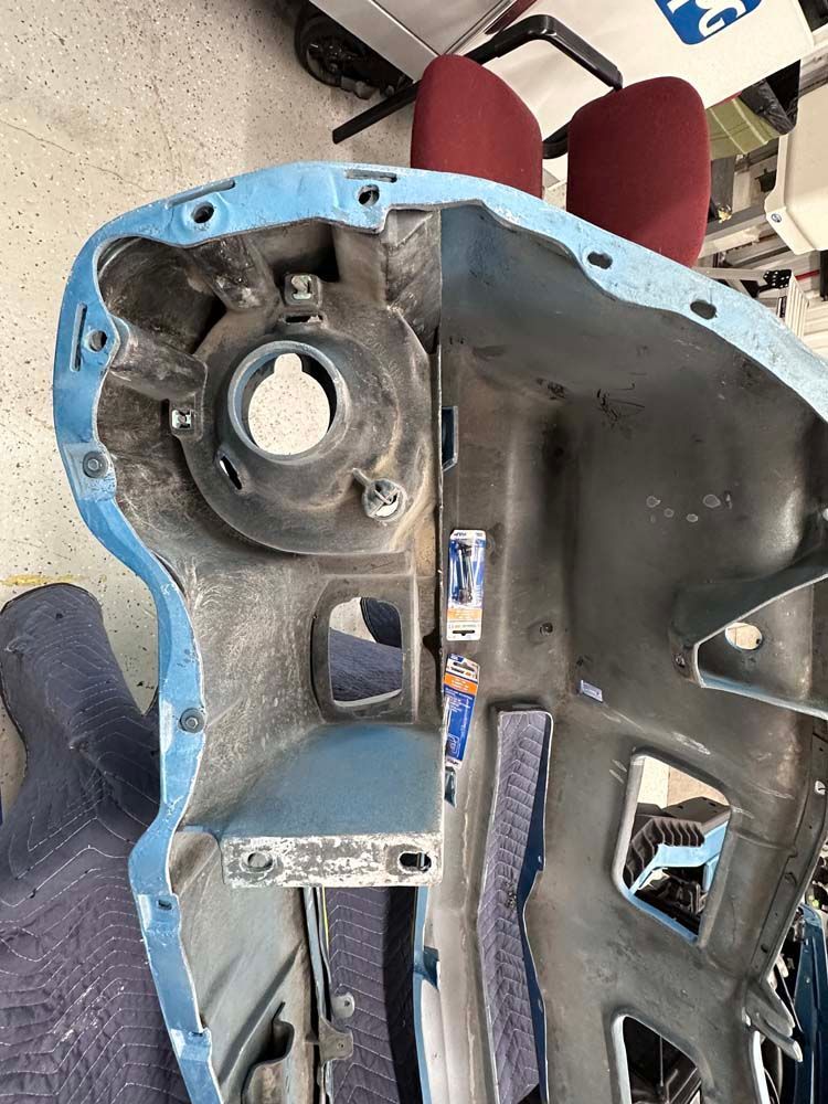 A blue car bumper is being removed from a car in a garage.