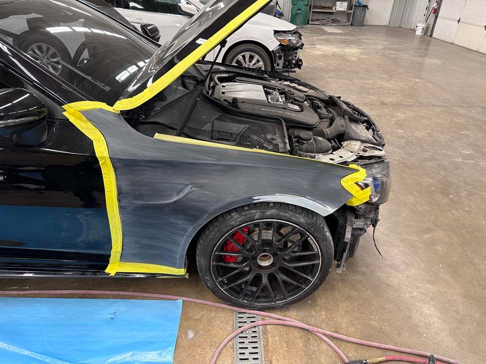 A black car with the hood up is being worked on in a garage.