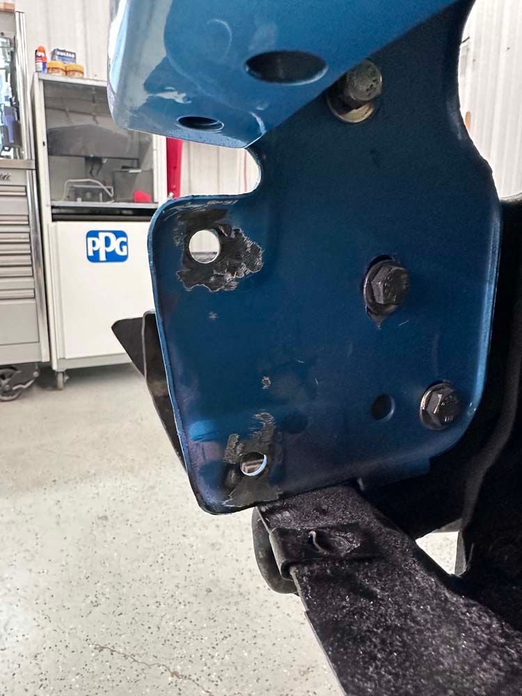 A blue car is sitting in a garage next to a sign that says ppg