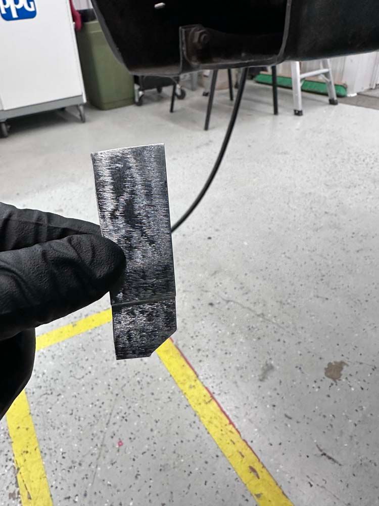 A person wearing black gloves is holding a piece of metal