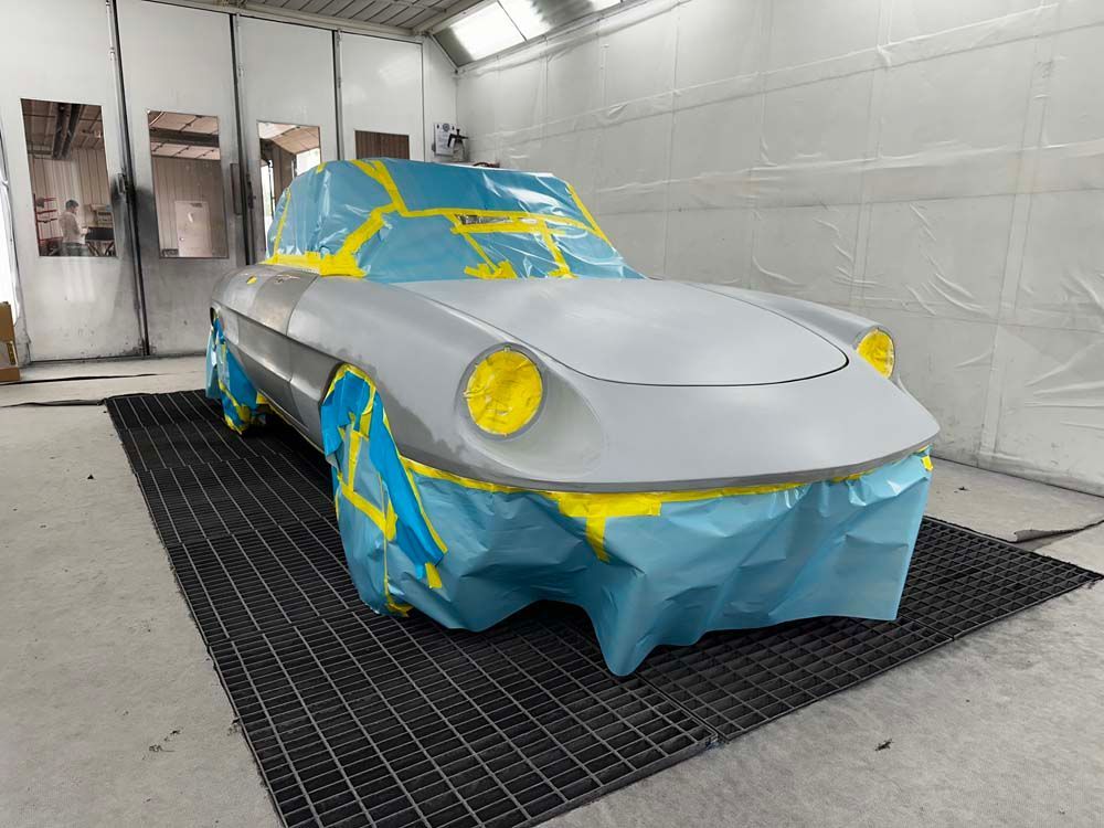 A car is covered in blue and yellow tape in a paint booth.